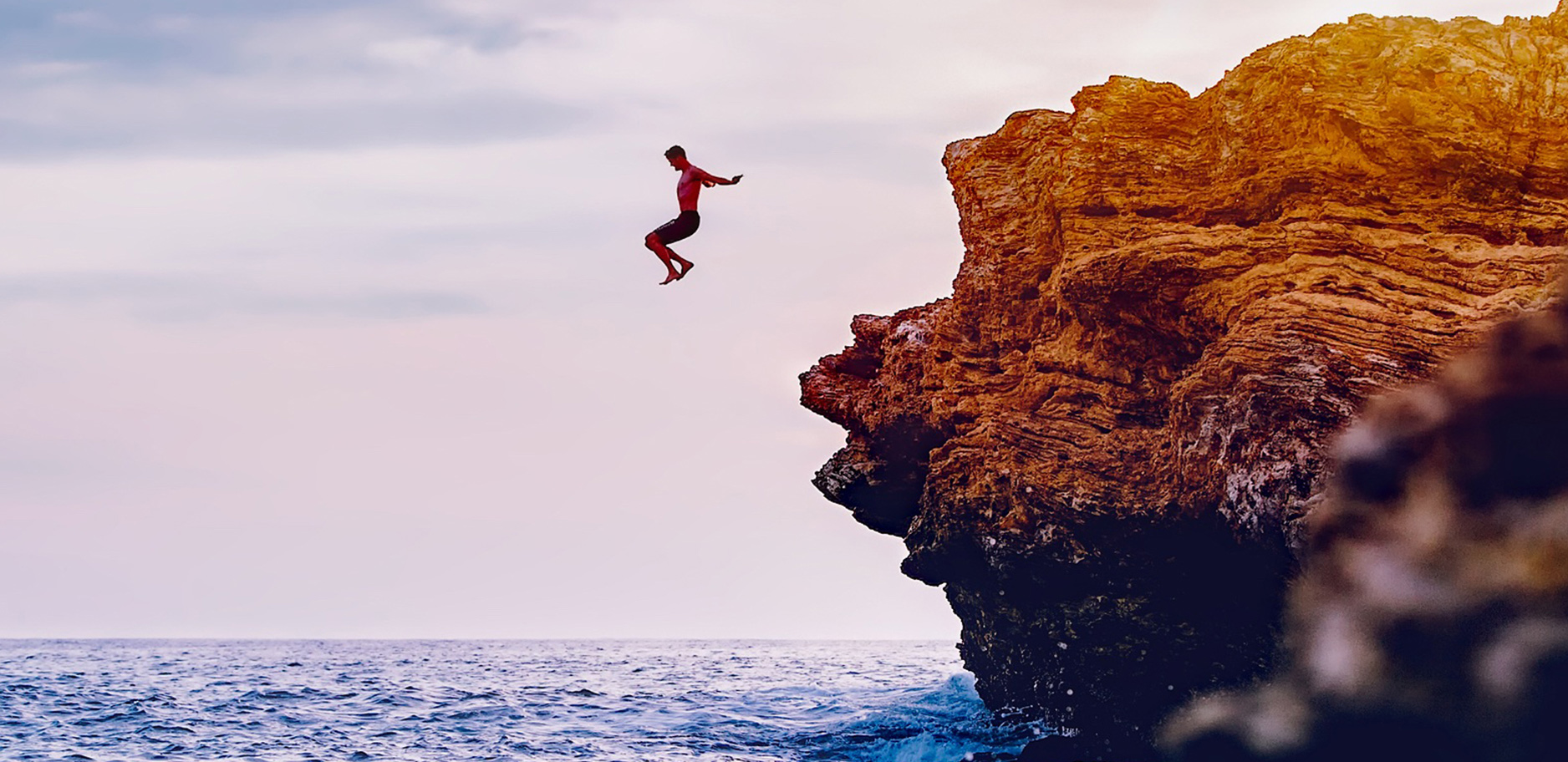 Man jumping off cliff into the sea