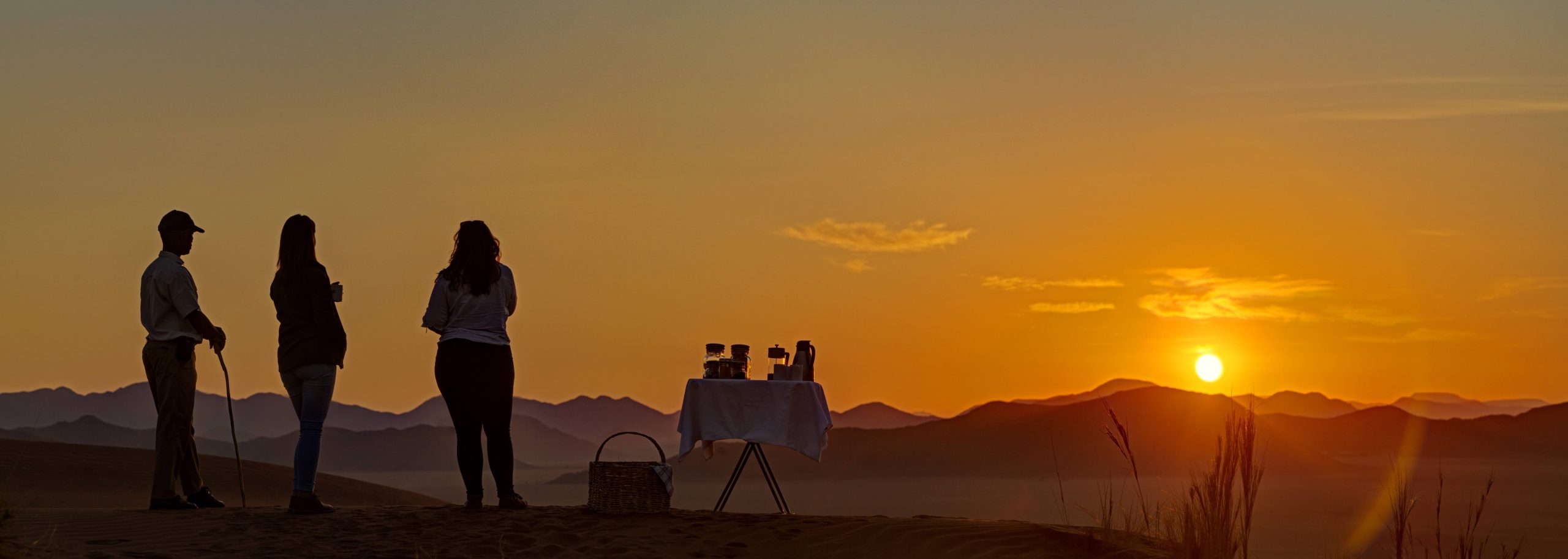 Three people on safari looking out to sunset